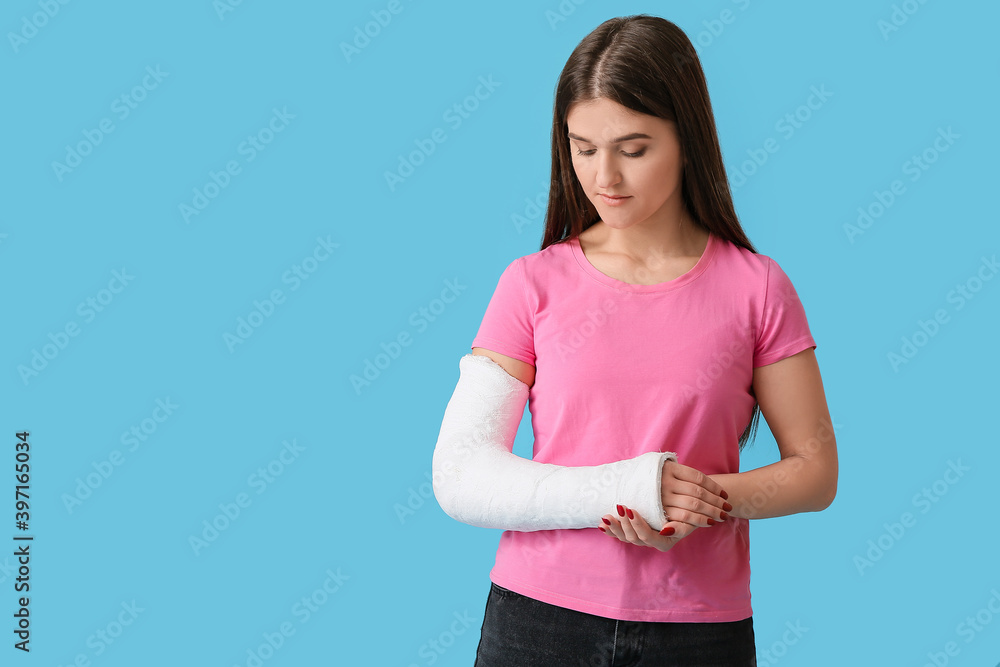 Young woman with broken arm on color background