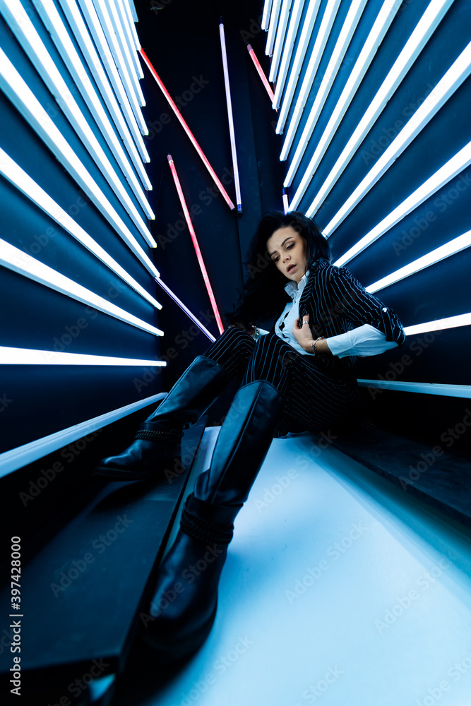 Disco lights in room. Girl in leather clthes poses to the camera. Brunette in futuristic interior.