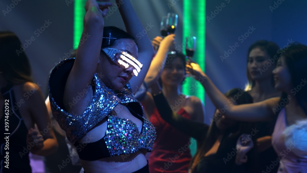 Group of people dance in disco night club to the beat of music from DJ on stage . New year night par