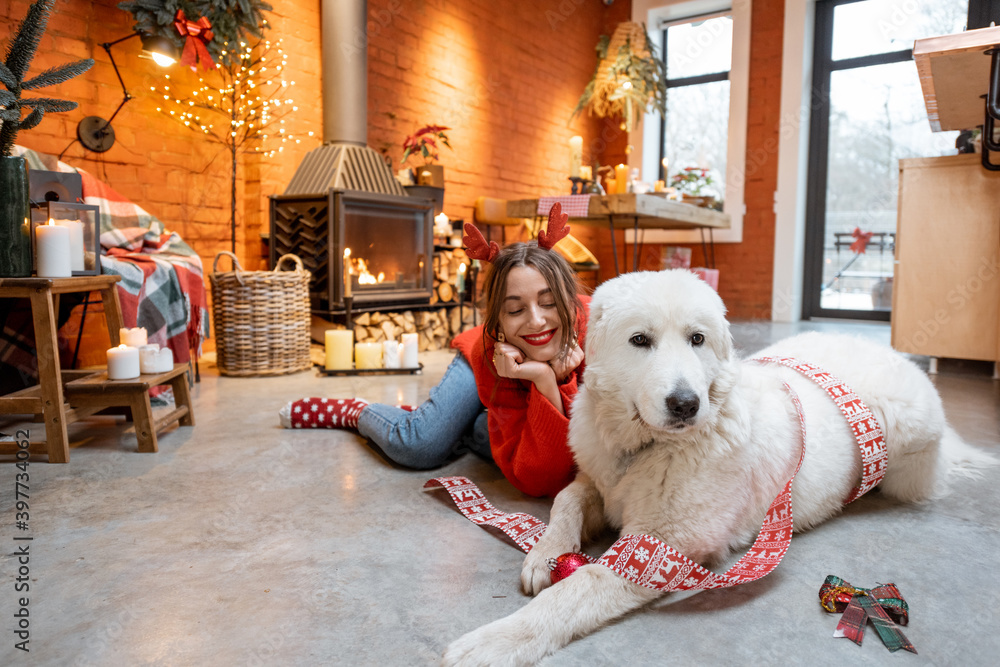 Young woman with her cute white dog during a happy New Year holidays sitting by a fireplace at home