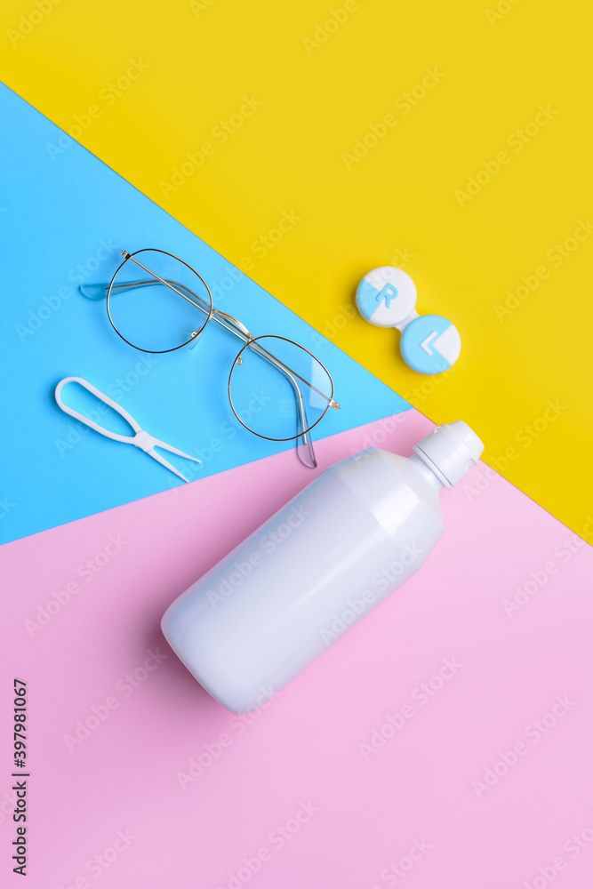 Container with contact lenses, solution, tweezers and eyeglasses on color background