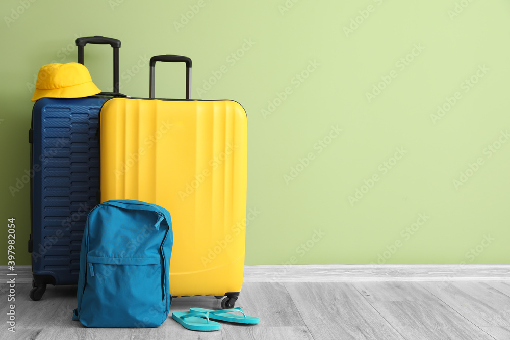 Packed suitcase with backpack and hat near color wall