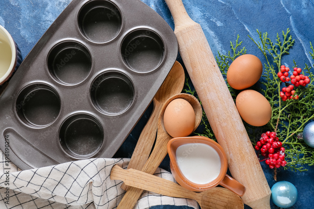 Ingredients for Christmas muffins and baking utensils on color background