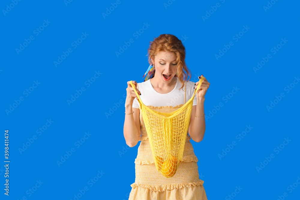 Beautiful young woman holding bag with oranges on color background