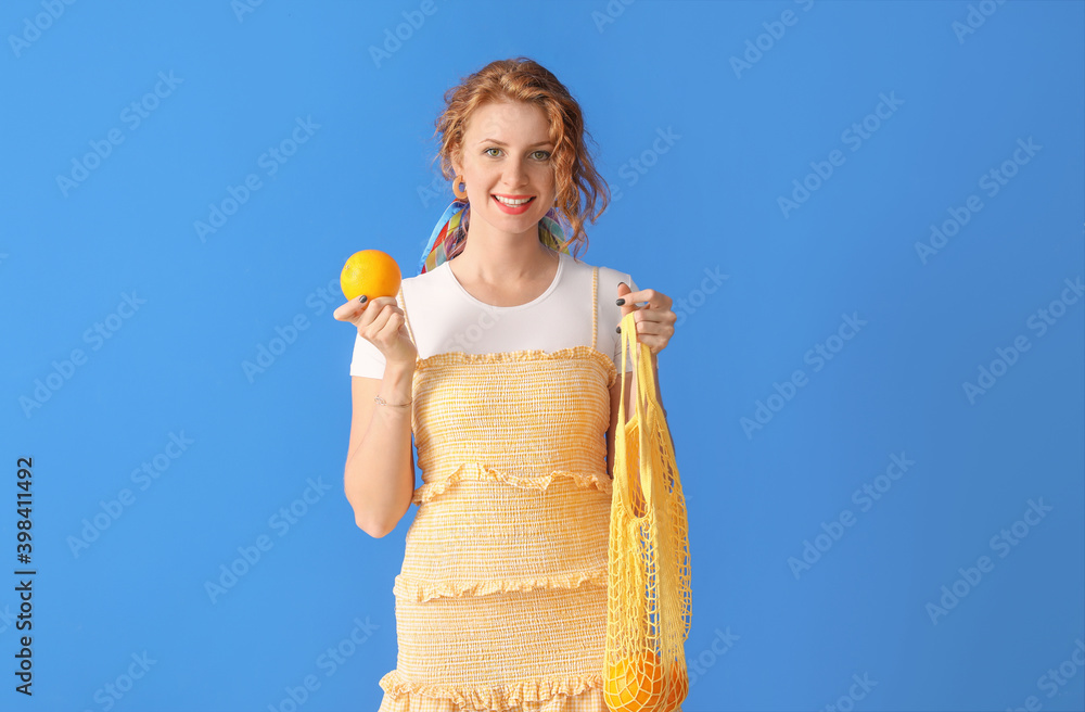 Beautiful young woman holding bag with oranges on color background