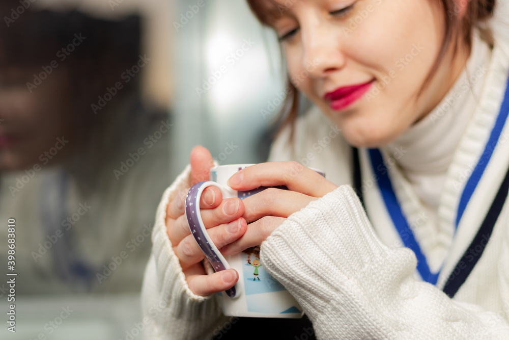 一个穿着温暖毛衣的年轻漂亮女孩坐在窗边的窗台上，手里拿着一杯咖啡