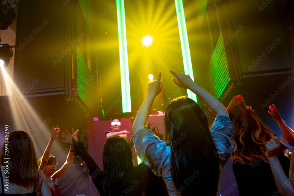 Group of people dance in disco night club to the beat of music from DJ on stage . New year night par