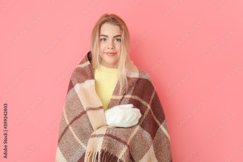 Young woman wrapped in warm plaid on color background. Concept of heating season