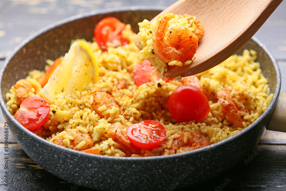 Frying pan with tasty pilaf and wooden spoon