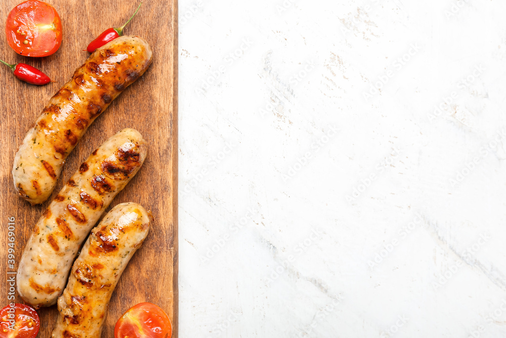 Wooden board with delicious grilled sausages and vegetables on light background