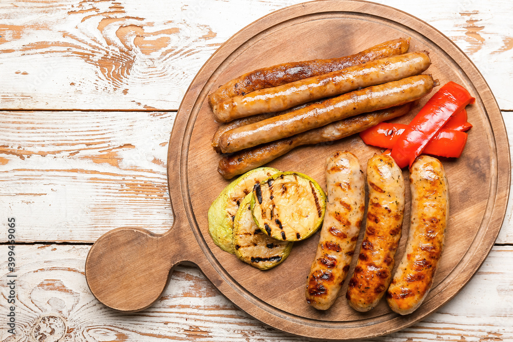 Wooden board with delicious grilled sausages and vegetables on table