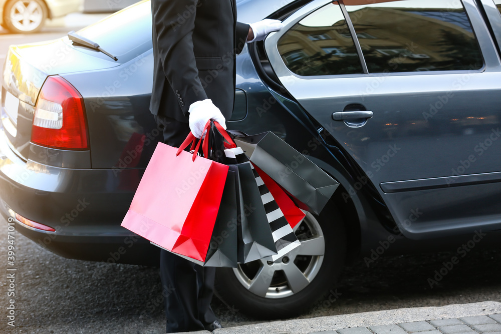 Chauffeur with shopping bags opening door of luxury car