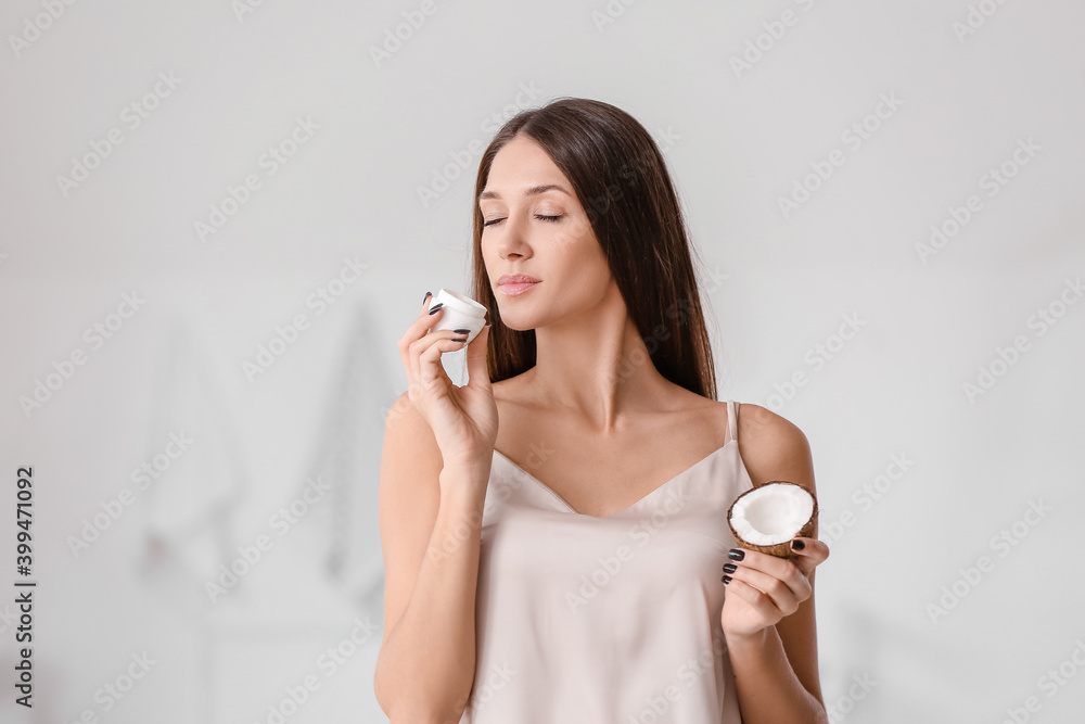 Beautiful young woman with coconut cream in bathroom