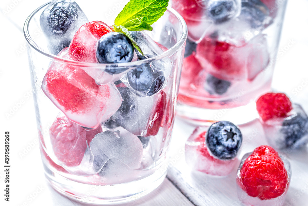 Ice cubes with blueberry and raspberry in glass on wooden table