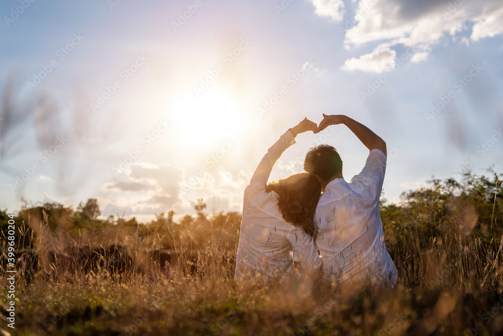 Happy romantic couple the sunset in the meadow love gesturing a heart with arm.