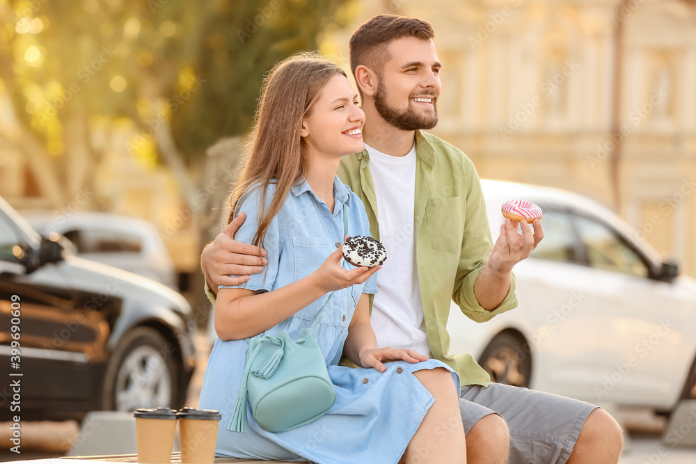 Young couple eating sweet donuts outdoors