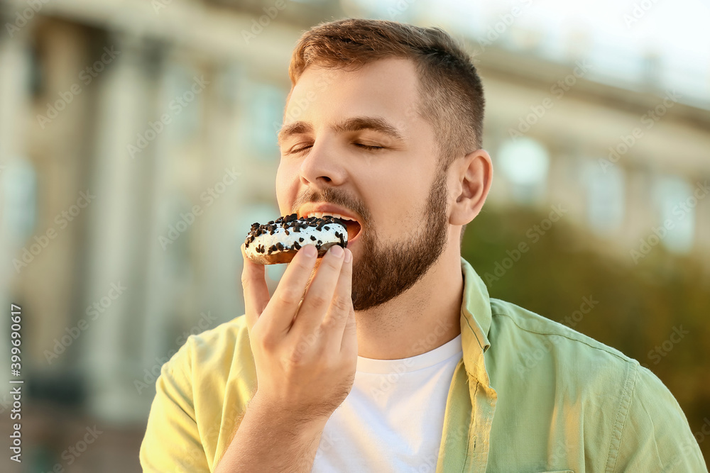 英俊的年轻人在户外吃甜甜圈