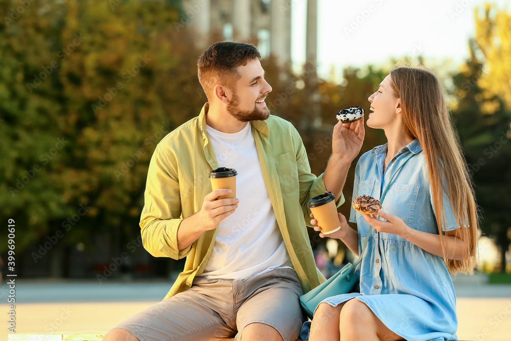 年轻夫妇在户外吃甜甜圈喝咖啡