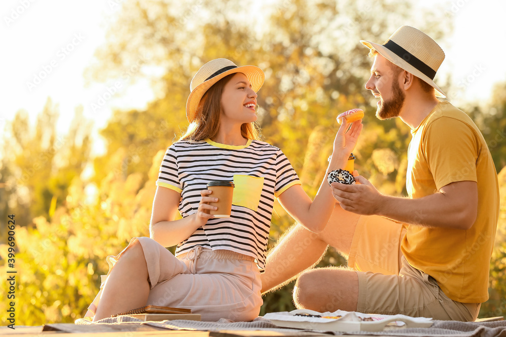 Young couple eating sweet donuts and drinking coffee outdoors