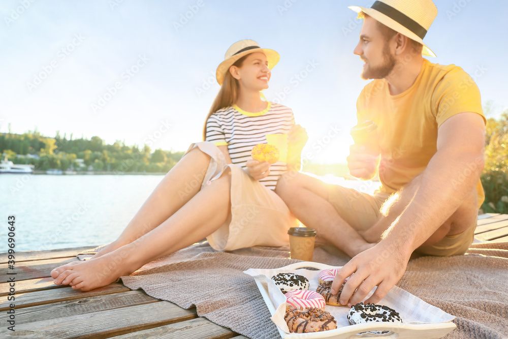 Young couple eating sweet donuts and drinking coffee near river