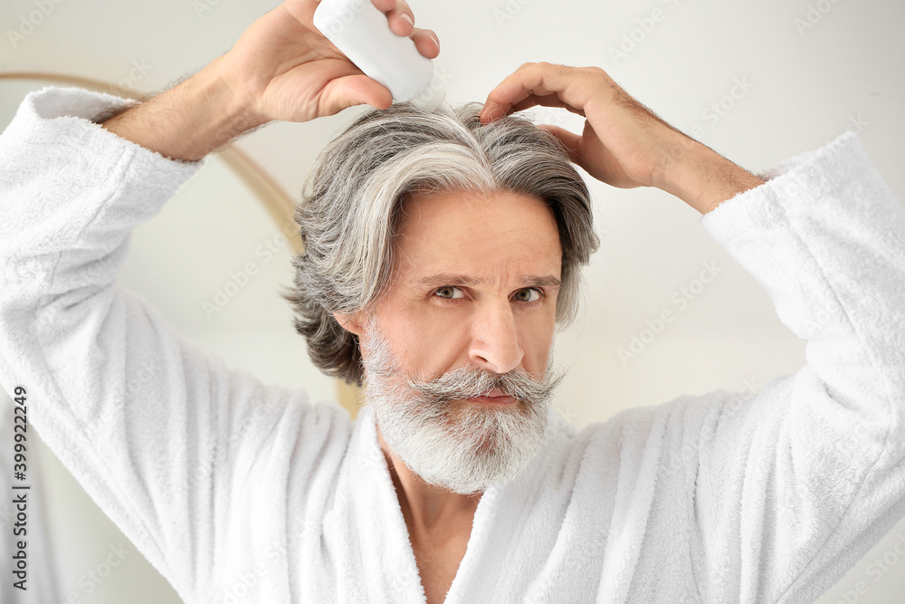 Mature man using serum for hair loss treatment near mirror