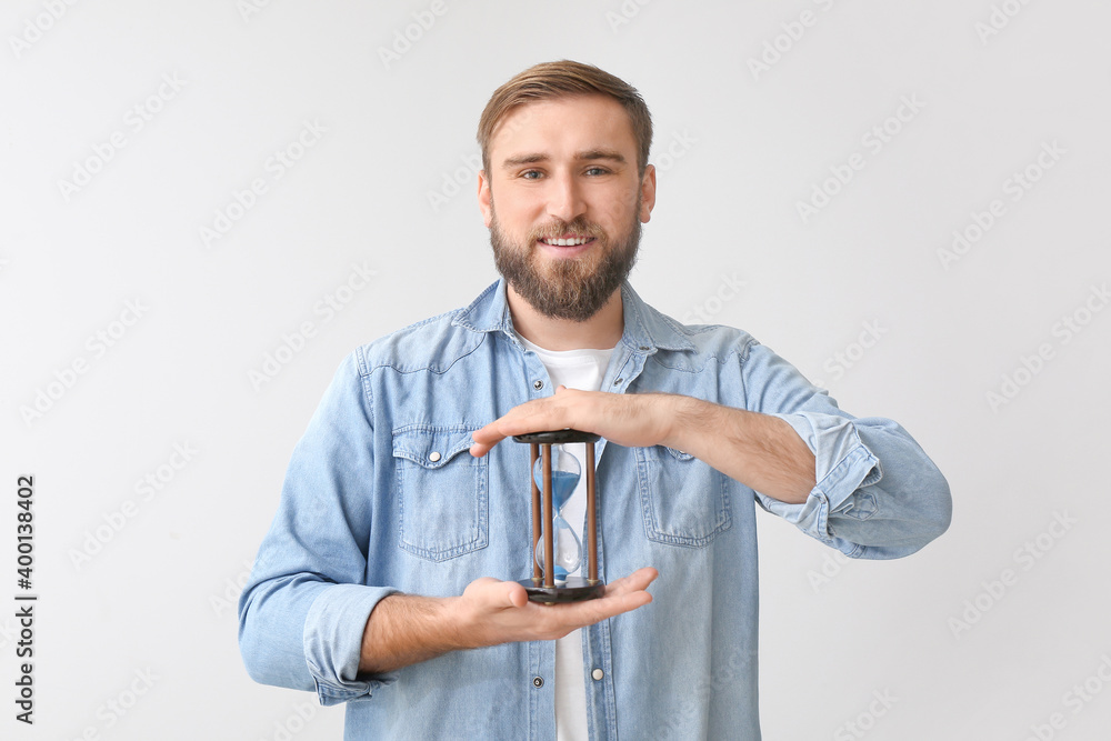 Young man with hourglass on light background