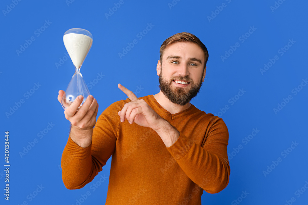 Young man with hourglass on color background