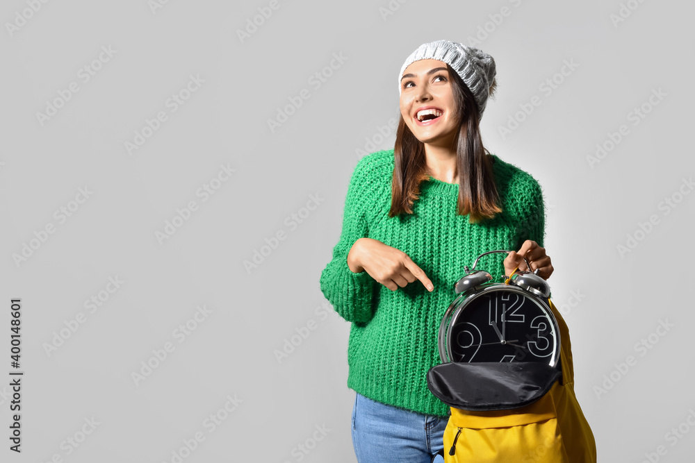 Female student with clock on grey background