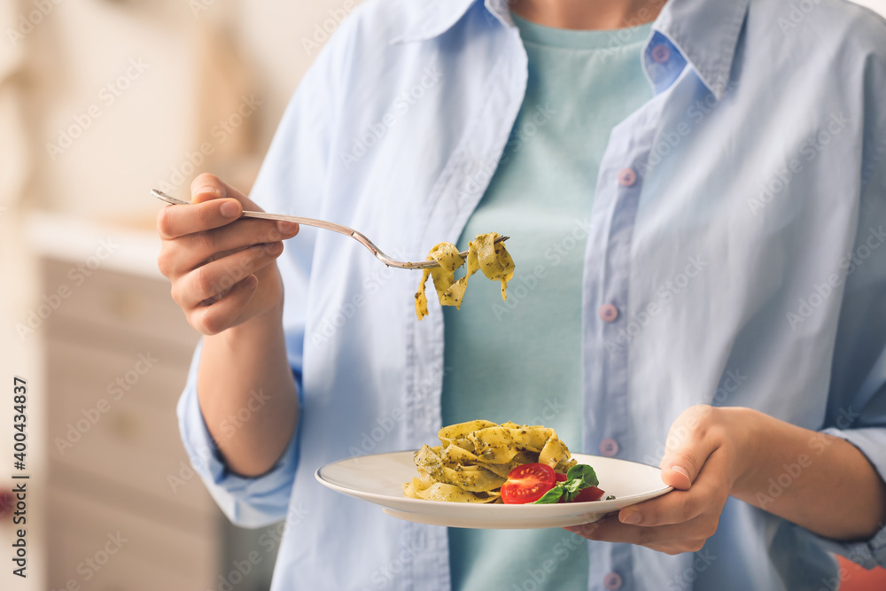 Woman eating pasta with pesto sauce in kitchen