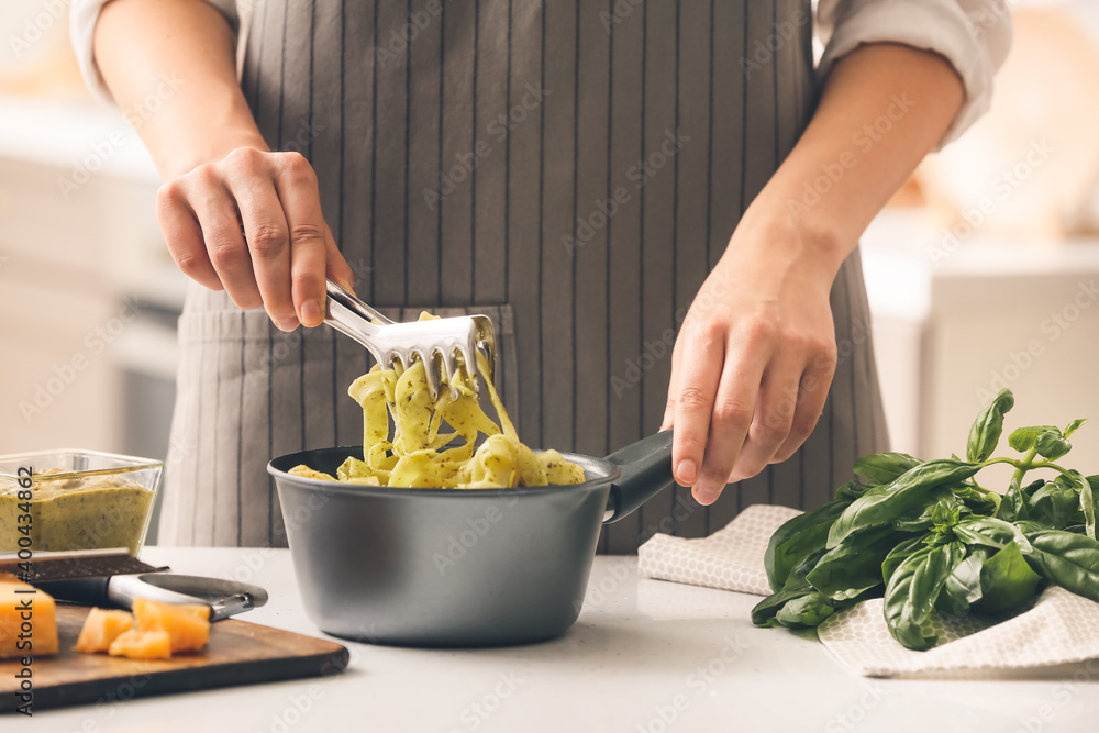 Woman cooking pasta with pesto sauce in kitchen