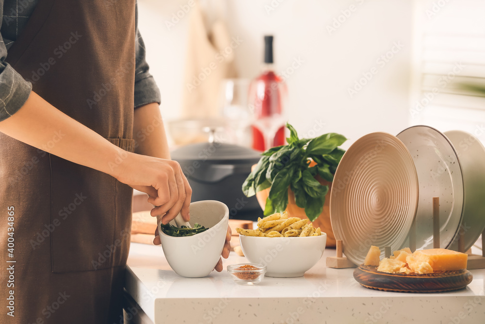 Woman cooking pasta with pesto sauce in kitchen