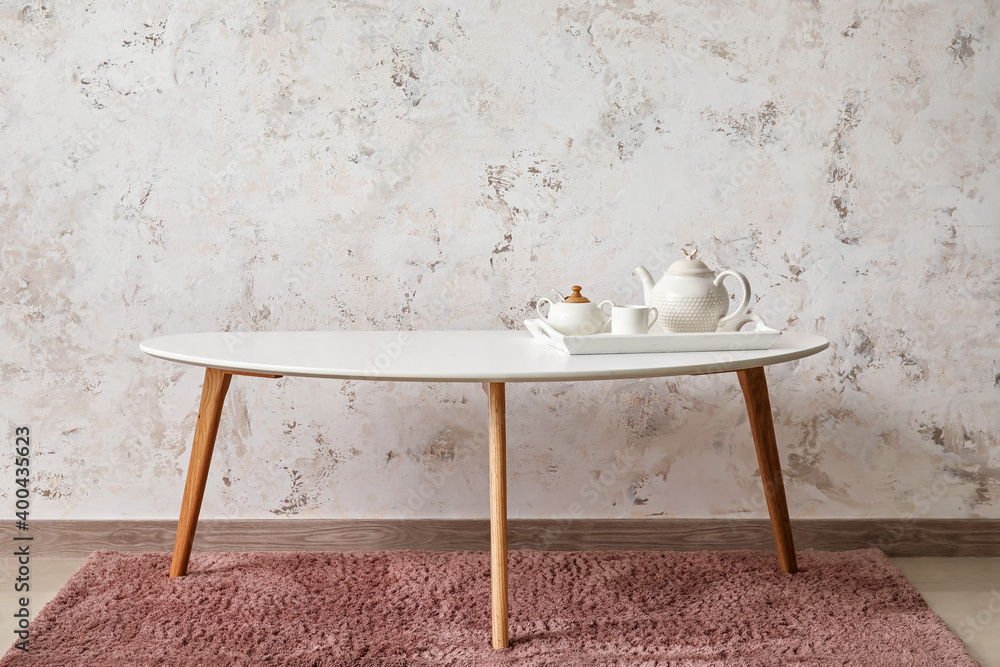 Tray with teapot and cups on stylish table near light wall in room