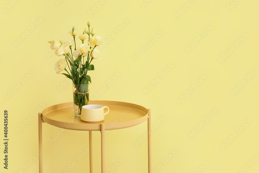 Stylish table with flowers and cup near color wall in room