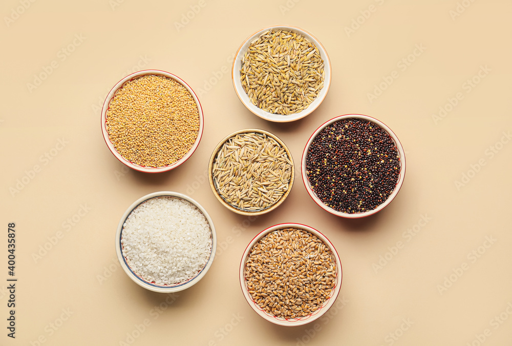 Bowls with assortment of cereals on color background