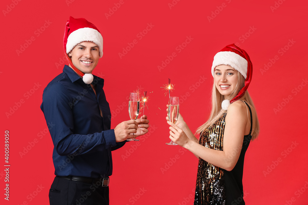 Happy young couple with Christmas sparklers and champagne on color background