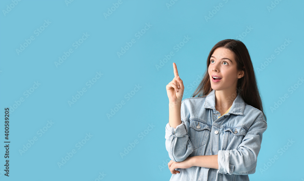 Portrait of beautiful young woman showing something on color background