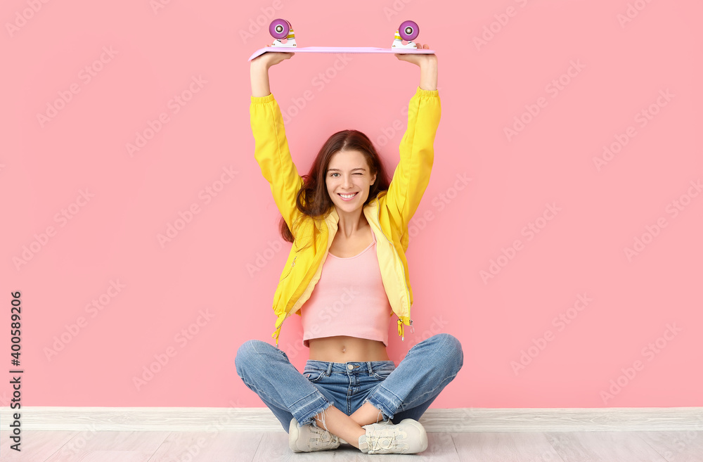 Young woman with skateboard sitting near wall