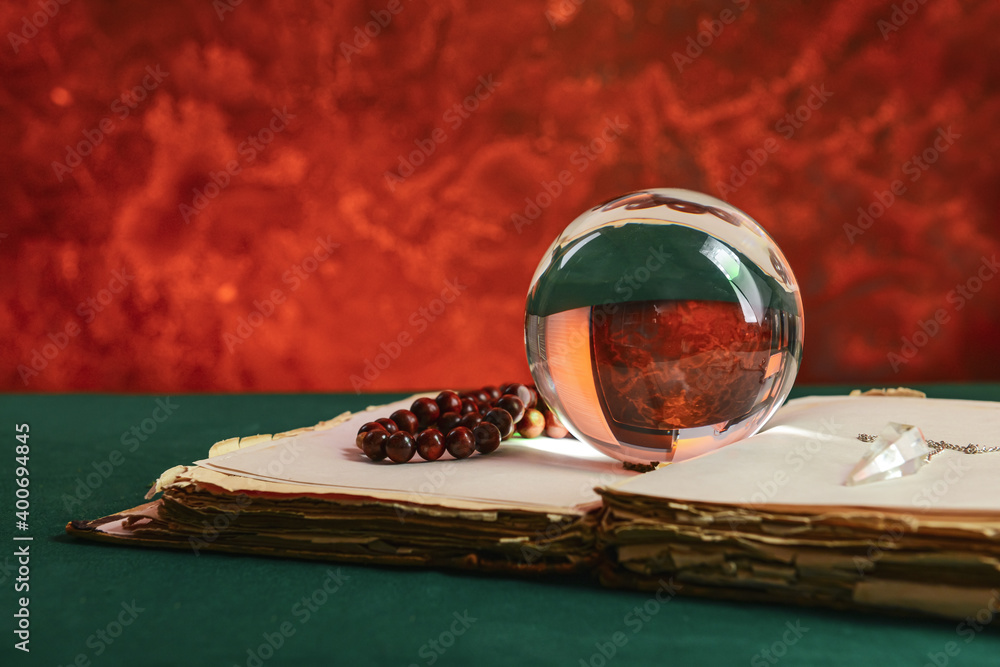 Spell book, crystal ball, pendulum and beads on table