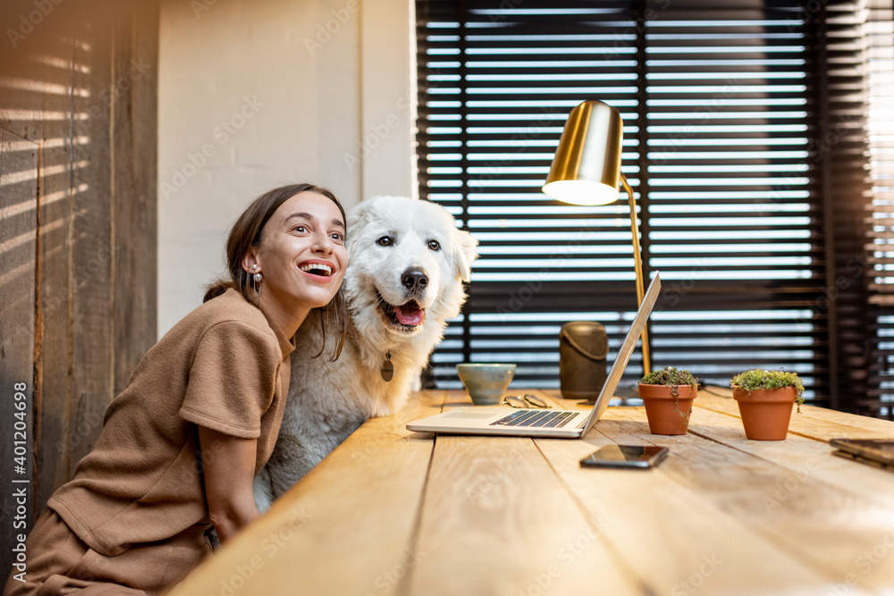 Portrait of a young woman and her cute white dog at the workplace in the home office