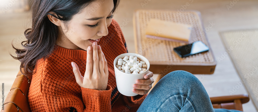 年轻漂亮的亚洲女人穿着毛衣，手拿着一杯咖啡，冬天早晨在何处放松