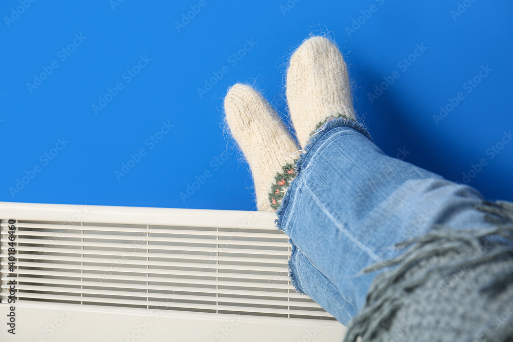 Mature woman warming legs near electric heater. Concept of heating season