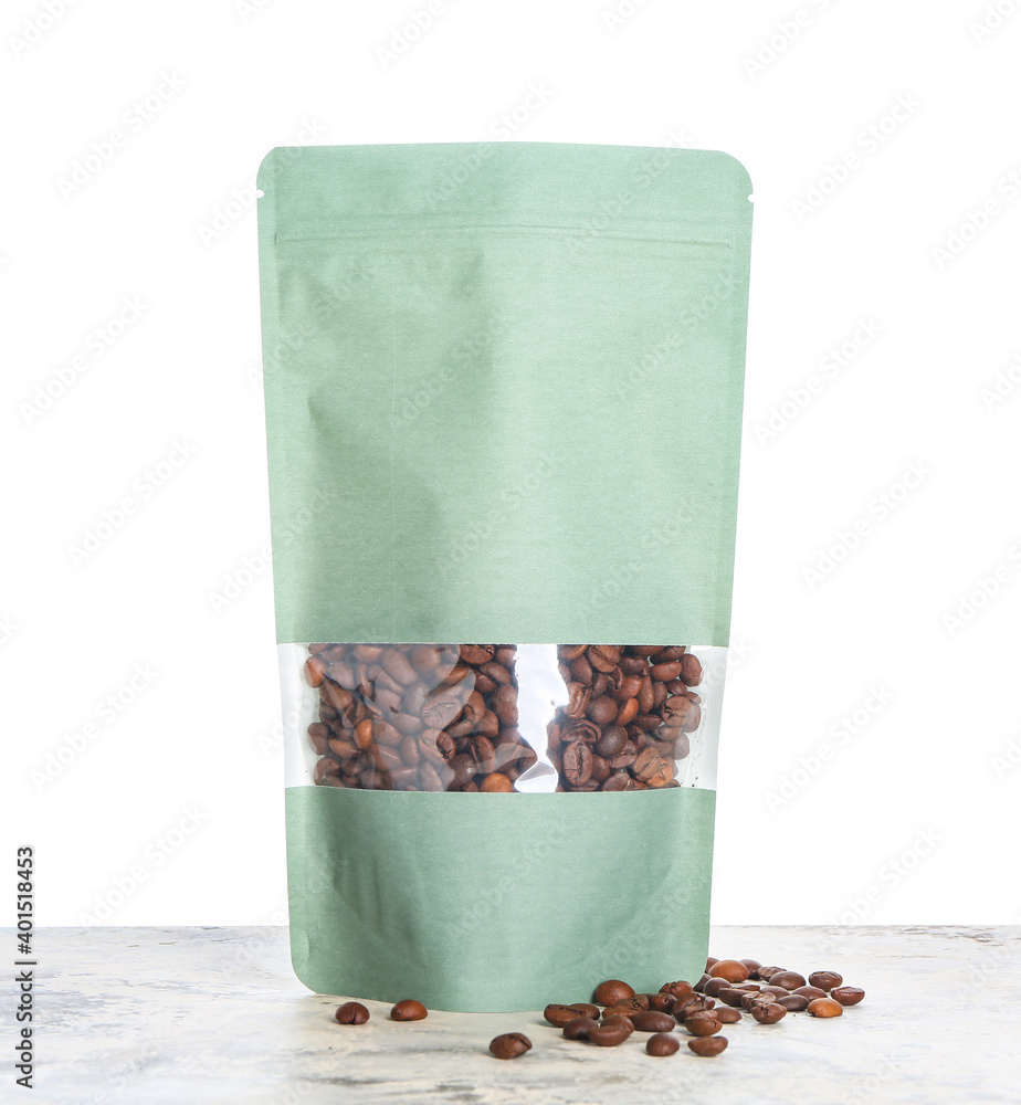 Bag with coffee beans on table against white background