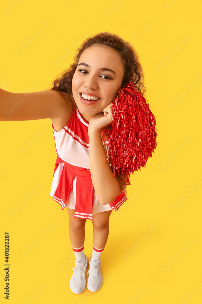 Beautiful young cheerleader taking selfie on color background