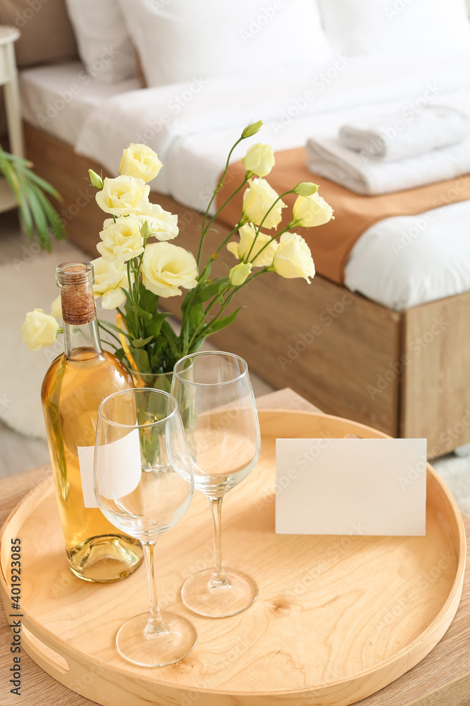 Tray with bottle of wine and glasses on table in hotel honeymoon room