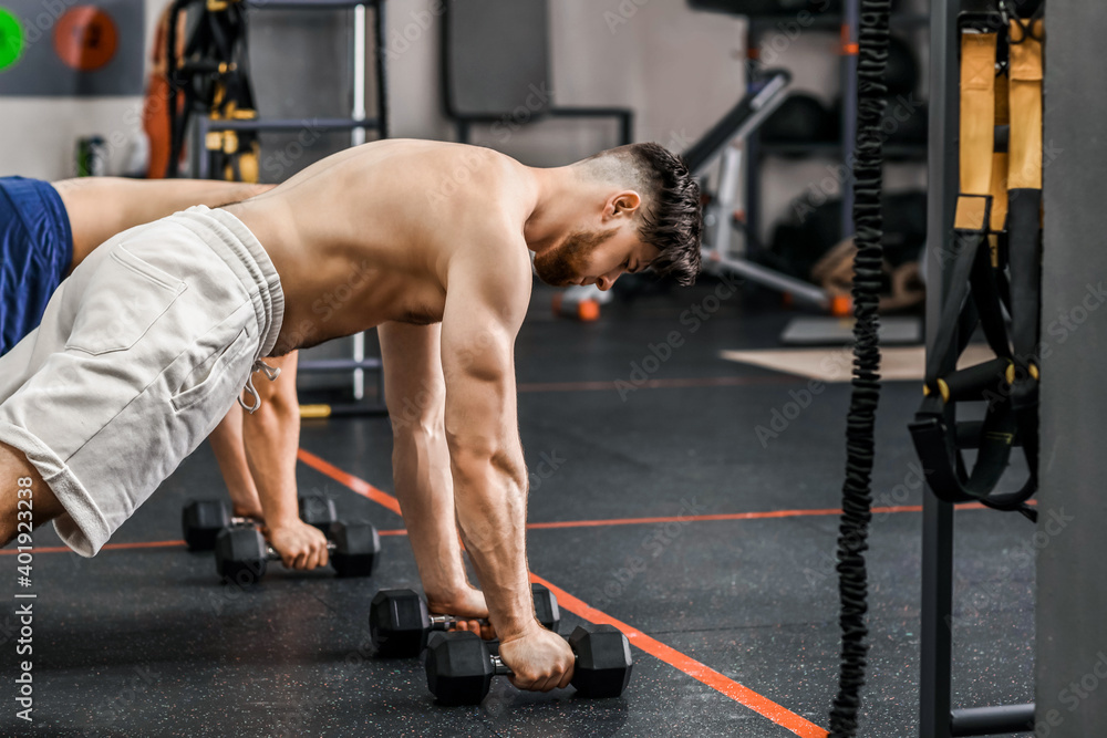 Handsome muscular men exercising with dumbbells in gym