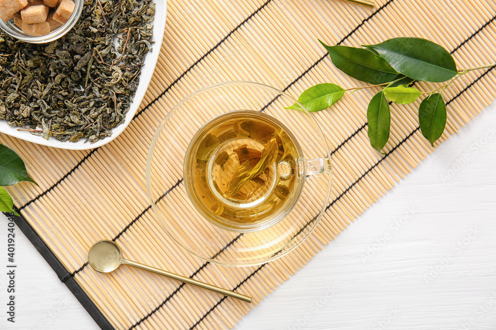 Cup of green tea and dry leaves on bamboo mat