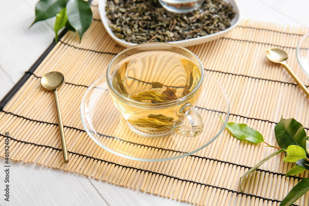 Cup of green tea and dry leaves on bamboo mat