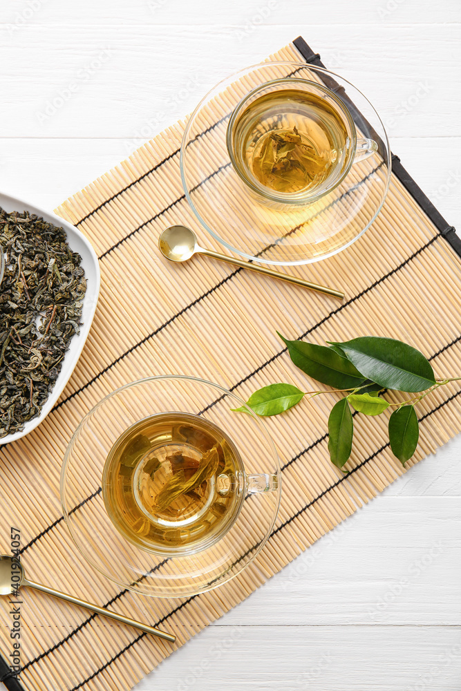 Cups of green tea and dry leaves on bamboo mat