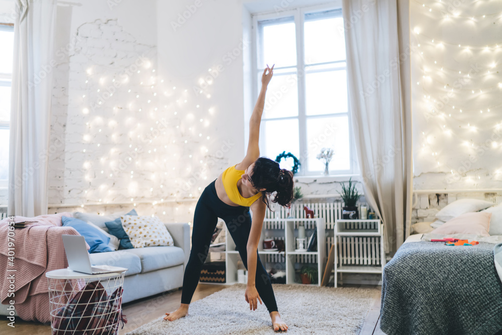 Flexible fit girl enjoying relaxation stretching exercising during morning time in cosy house interi