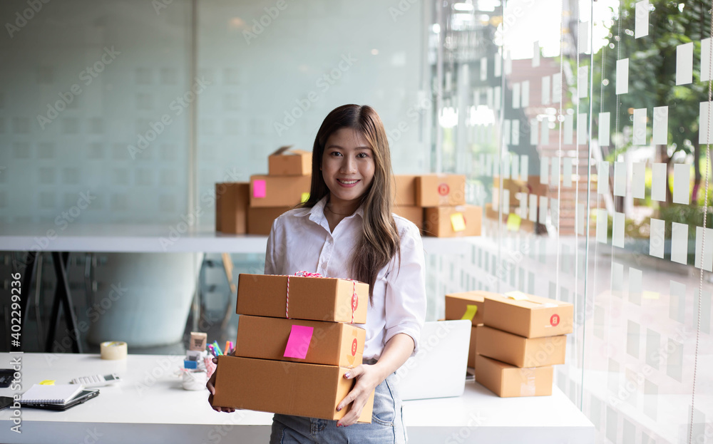 An Asian owner holds a package in a brown box, ready for delivery to a customer who orders online. A